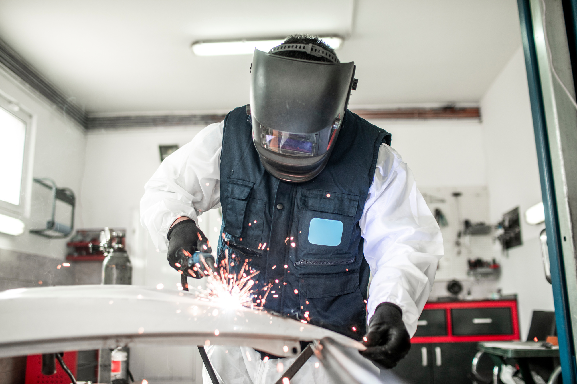 Car body shop technician using a MIG welder to repair a damaged car part in a car body shop